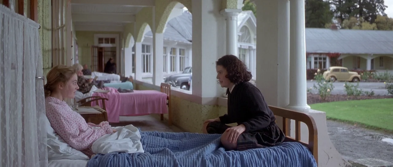 Heavenly Creatures (1994) movie still: medium — An open-air recovery porch with arched white columns features multiple single beds for patients. Two…