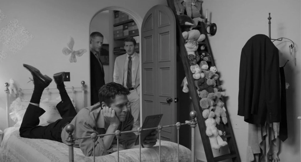 Much Ado About Nothing (2012) movie still: medium — A bedroom filled with children's stuffed animals and an arched doorway in the back. One man lies…