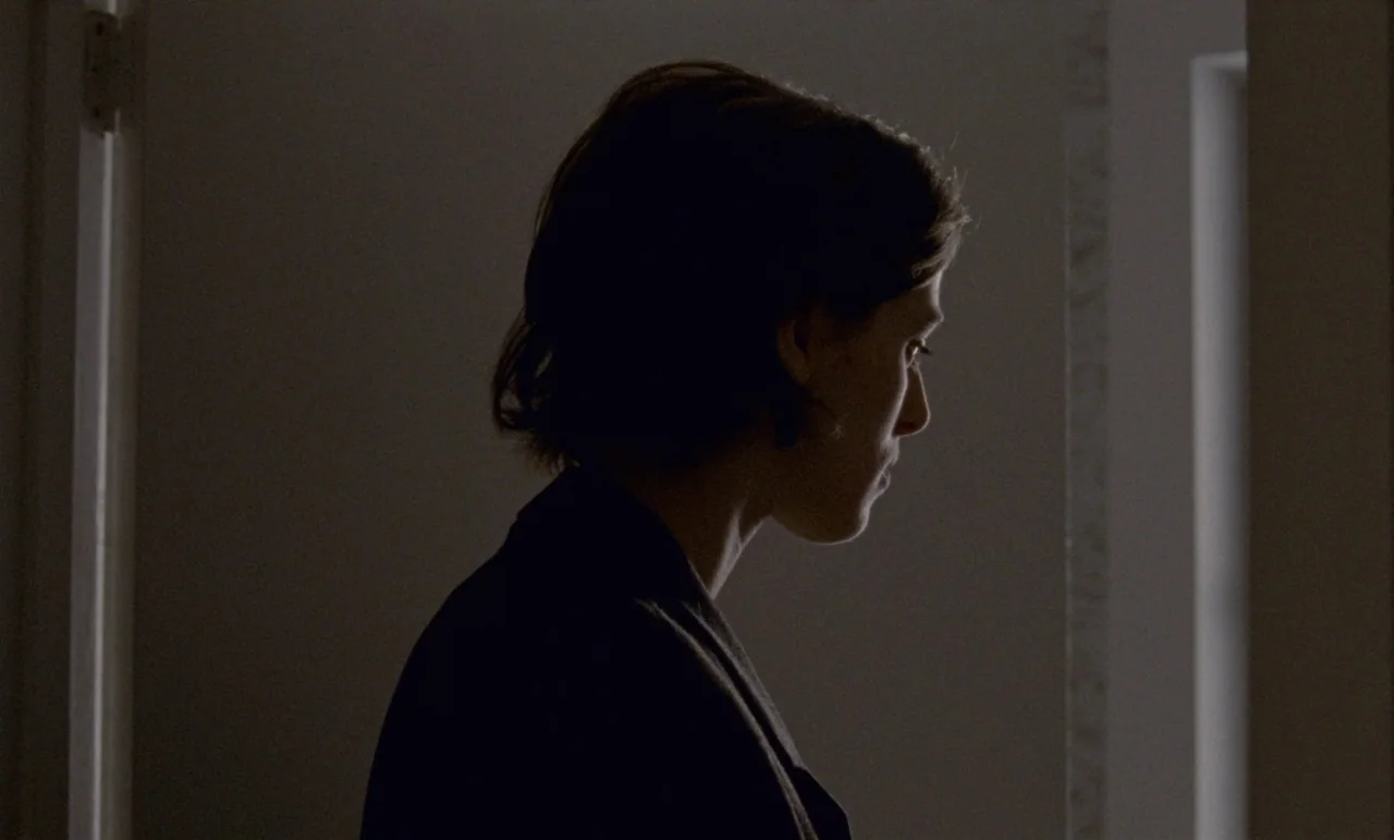 The Souvenir: Part II (2021) movie still: closeup — A woman stands in a dark doorway with a sliver of light to her side. She is captured in profile…