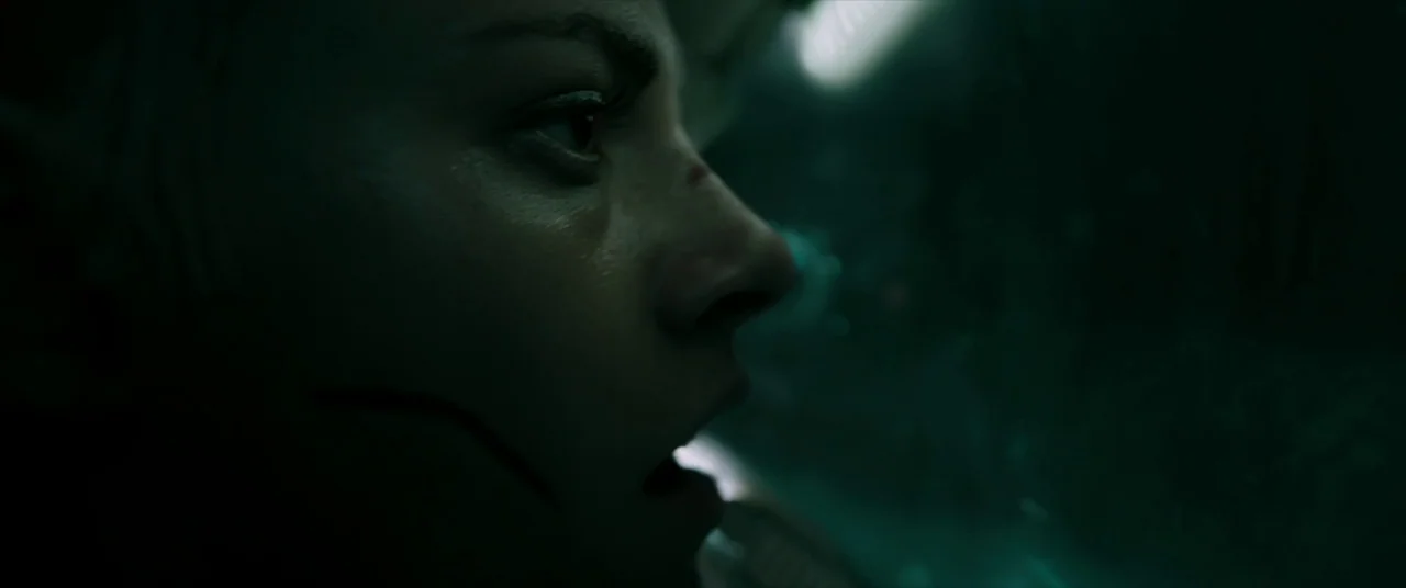 Underwater (2020) movie still: closeup — A dark, cramped metallic environment lit by dim, cool-toned fluorescent light sources. A woman with a small…