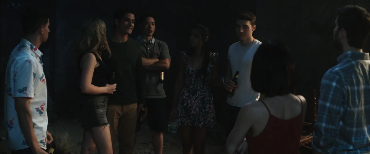 Truth or Dare (2018) movie still: medium — A group of young adults stands in a circle on sand at night. They are talking to each other while holding…