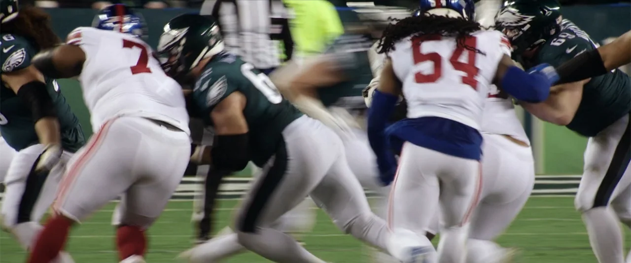 Kelce (2023) movie still: medium — An American football field during a professional game under bright stadium lights. Multiple players in opposing…