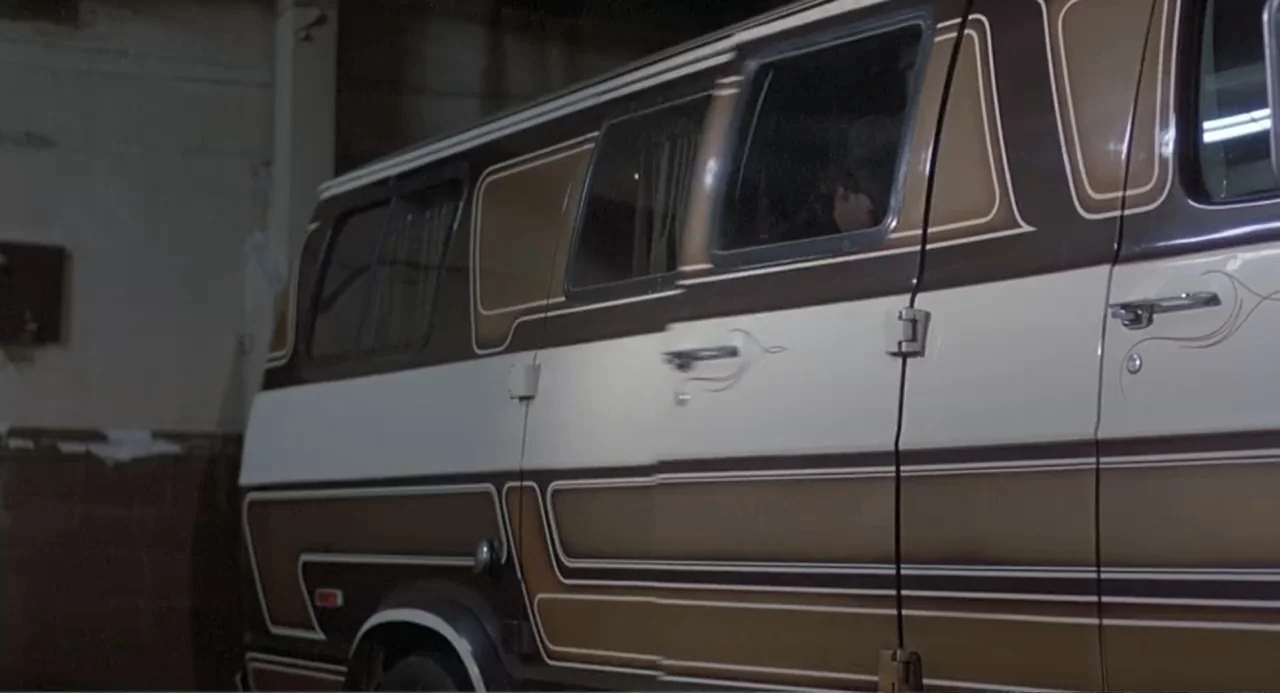 Death Wish II (1982) movie still: medium — A brown and white custom 1970s van sits inside a dimly lit concrete space. A person sits in the driver…