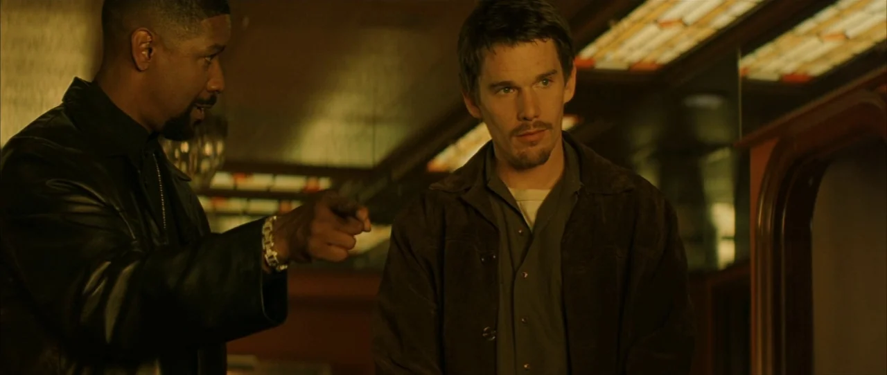 Training Day (2001) movie still: medium — A dark, dimly lit booth in a diner with reflective panels above. One man points his finger across the…