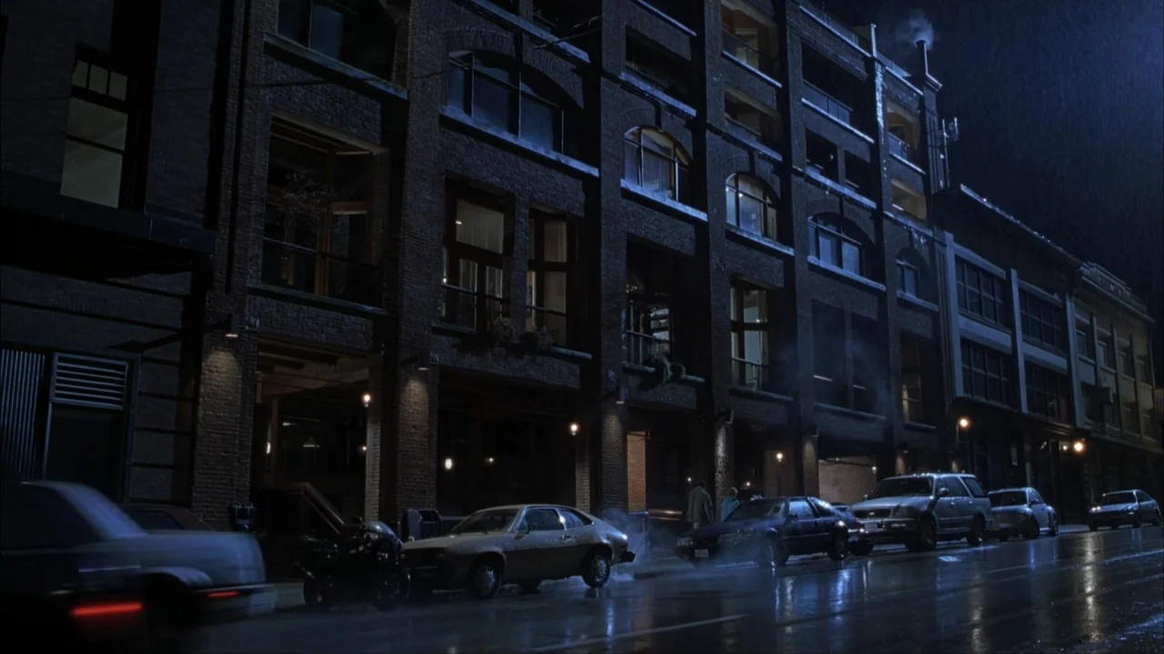 Final Destination 2 (2003) movie still: establishing — A multi-story brick industrial building occupies a dark city street during a rainstorm.…