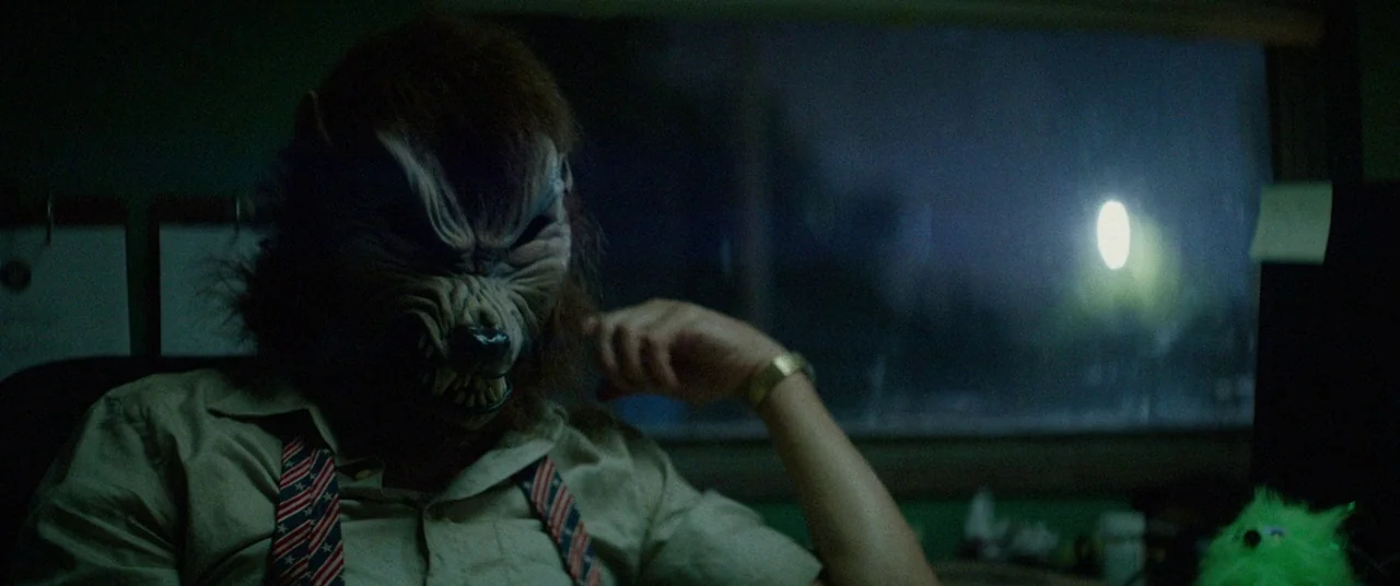 Triple 9 (2016) movie still: medium — A dimly lit, shadowed space contains a figure wearing a realistic, frightening wolf mask. The masked subject…