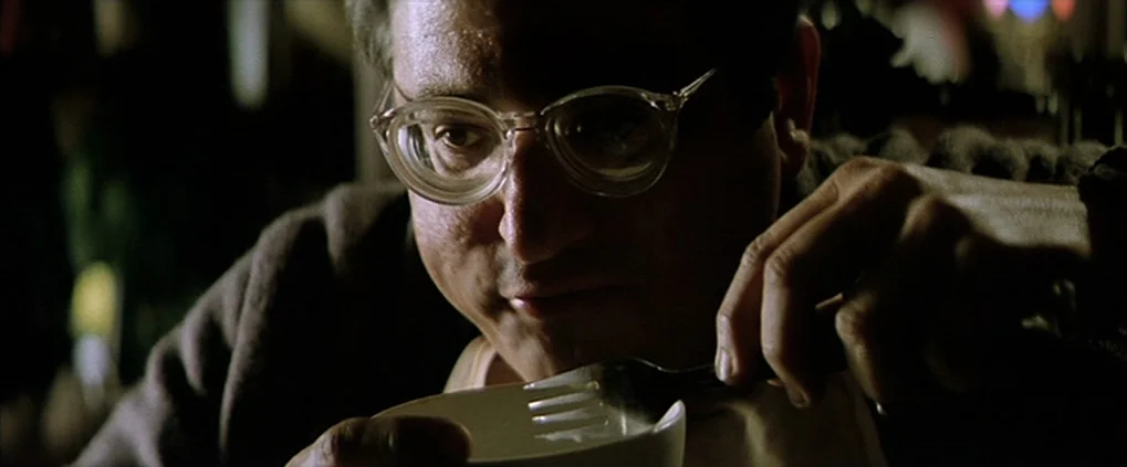 Anguish (1987) movie still: closeup — A dimly lit room provides the backdrop for a close-up of a man eating. He holds a small ceramic bowl and uses…