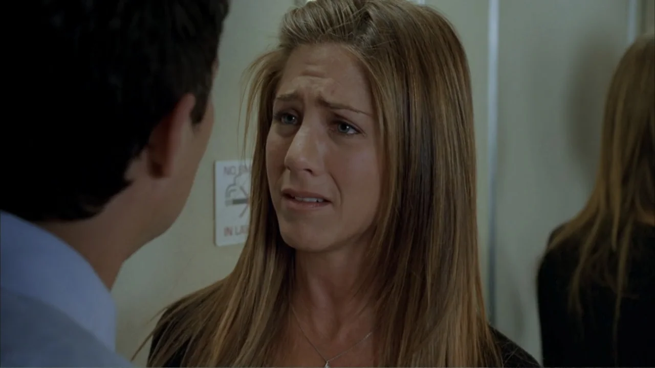Rumor Has It... (2005) movie still: closeup — A close view inside an elevator with a cream-colored wall and signage behind. A woman speaks to a man…