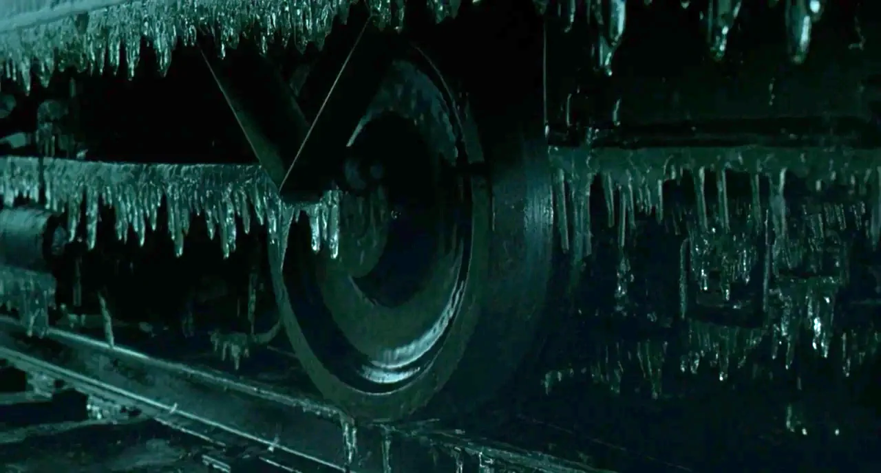 The Ice Storm (1997) movie still: closeup — A close view of a heavy metal train wheel assembly covered in frozen ice. Long icicles hang from the…