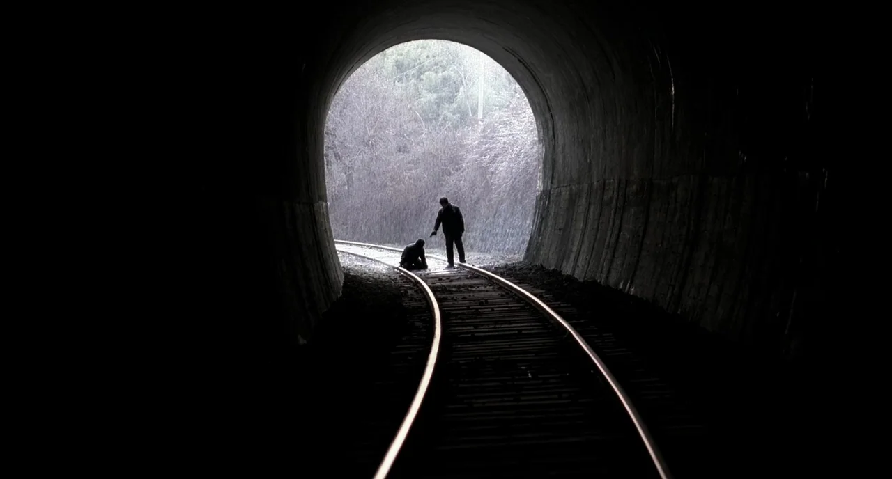 Memories of Murder (2003) movie still: wide — A concrete tunnel opens onto a brush-filled landscape with railway tracks leading out. Two individuals…
