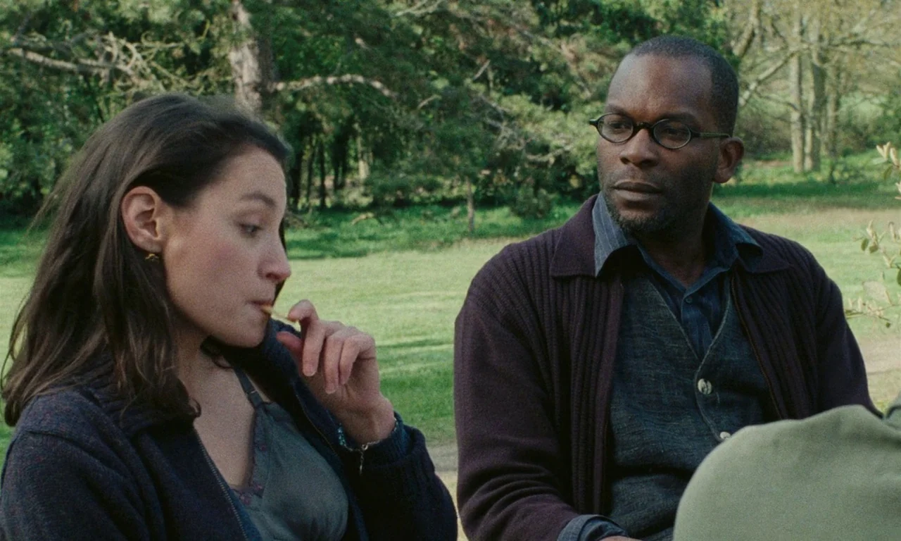 Late August, Early September (1998) movie still: medium — A grassy park with scattered trees provides a peaceful backdrop for conversation. A woman…