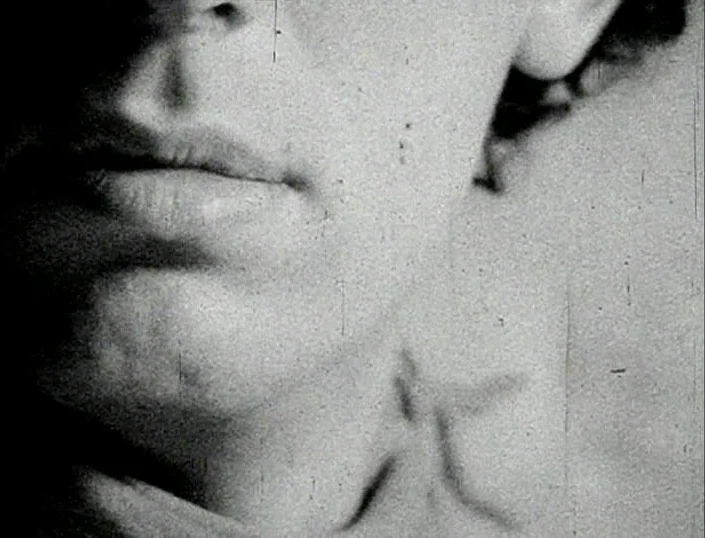 Glitterbug (1994) movie still: closeup — A close-up view of a face partially obscured by deep shadow and film grain. The skin texture shows through…