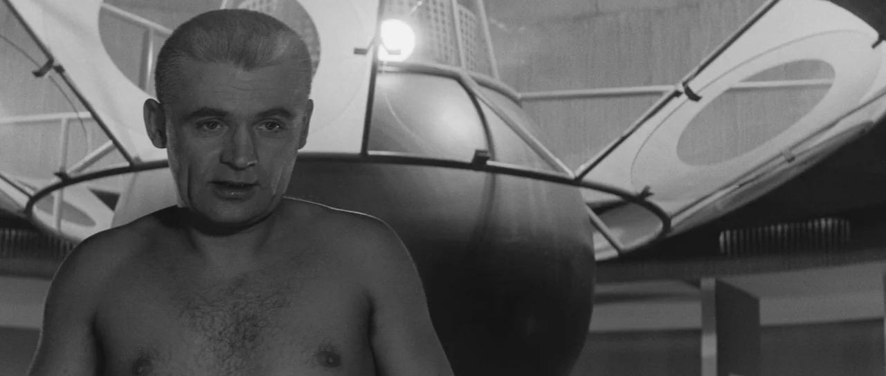 Ikarie XB 1 (1963) movie still: medium — A 1960s science fiction set features metallic curved surfaces and white ringed structures. A shirtless man…