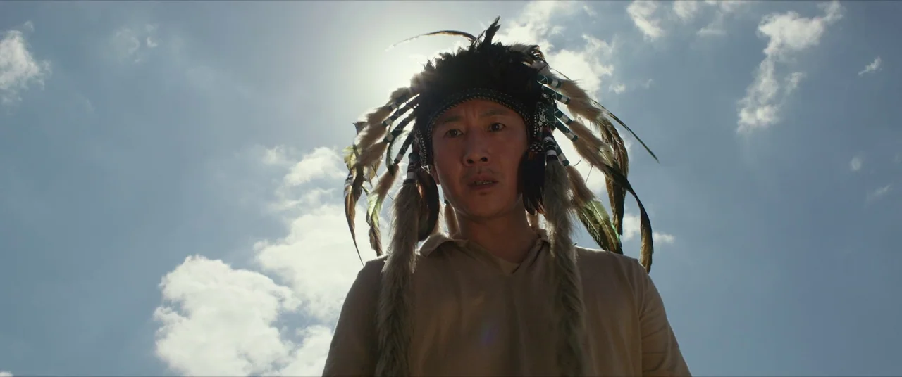 Parasite (2019) movie still: medium — An open sky with scattered white clouds serves as the background for a man. A man wearing a traditional…