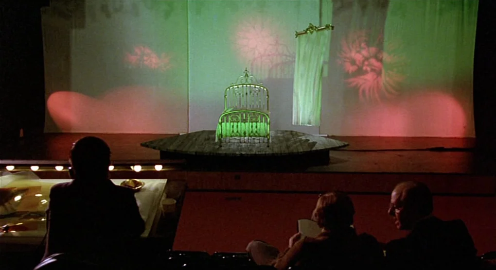 All That Jazz (1979) movie still: wide — A dark theater auditorium faces a small stage with a single white metal bed. Three people sit in the…