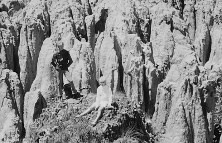 Fando y Lis (1968) movie still: fullbody — A rugged landscape filled with tall, eroded stone pillars and sparse patches of grass. A man stands…