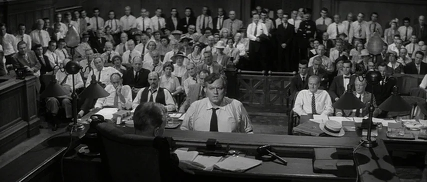 Compulsion (1959) movie still: wide — A crowded 1940s courtroom features wooden benches packed with spectators and legal counsel. A man stands in…
