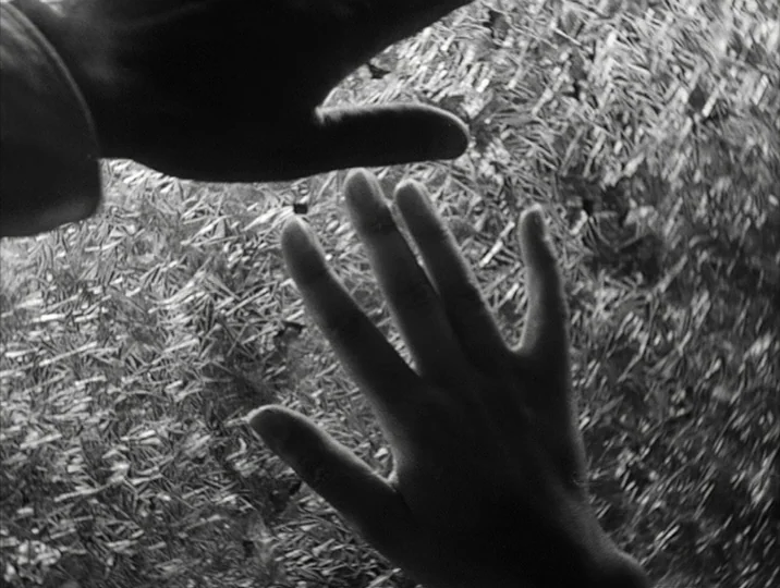 To Joy (1950) movie still: closeup — Two human hands press against a highly textured, semi-opaque patterned glass surface. The fingers are splayed…