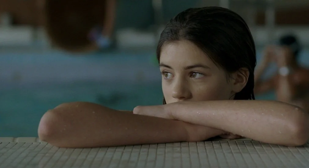 Water Lillies (2007) movie still: closeup — A teenage girl rests her arms on the tiled edge of an indoor pool. Her wet face is visible above her…