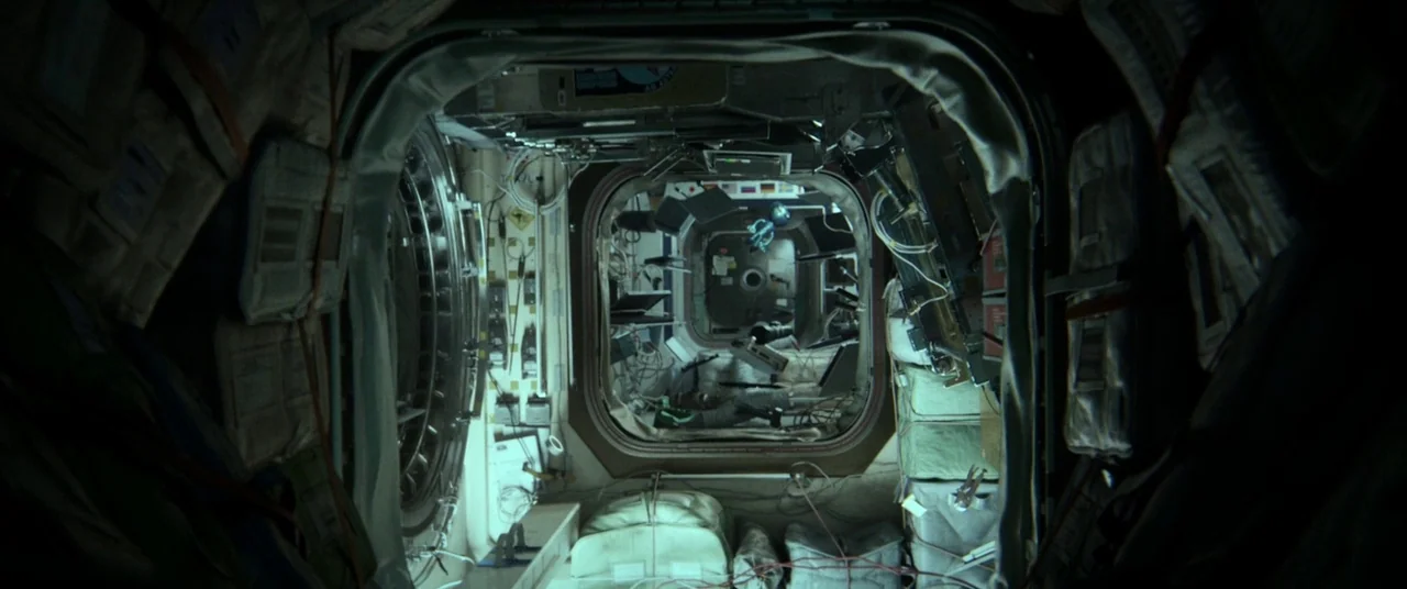 Gravity (2013) movie still: wide — The interior of a pressurized space station module features padded walls and technical equipment. A narrow…