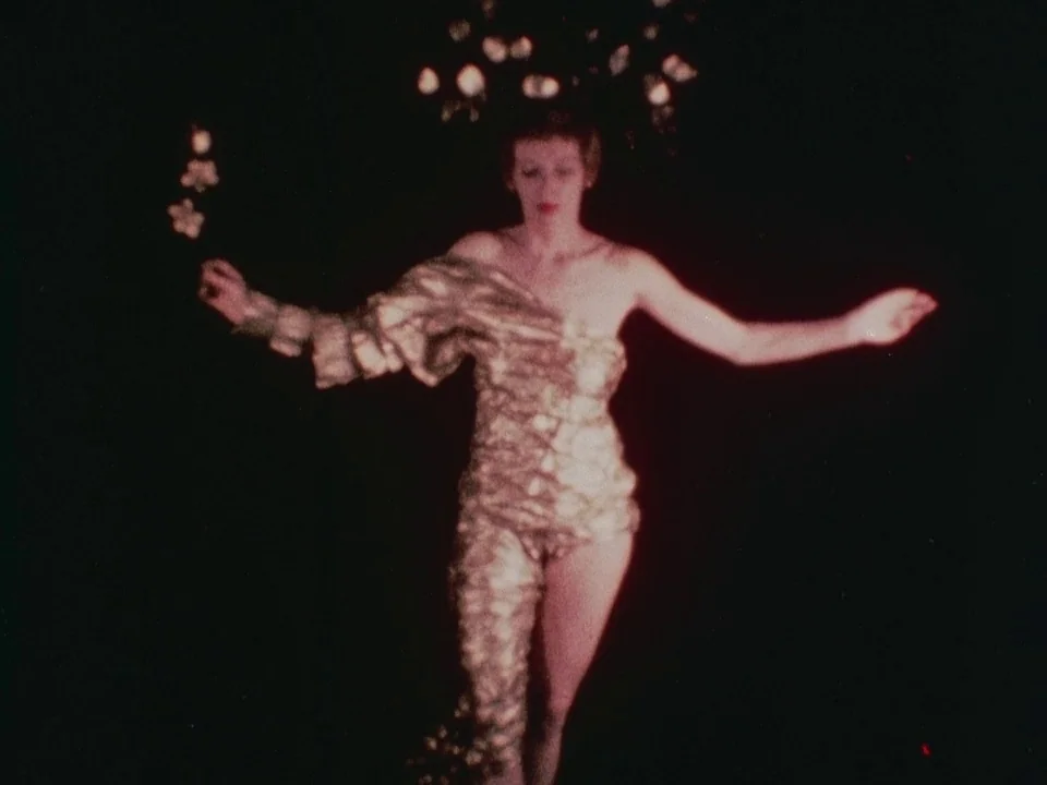 The Wormwood Star (1956) movie still: medium — A woman stands in the center of a pitch-black stage environment. She poses with arms extended while…