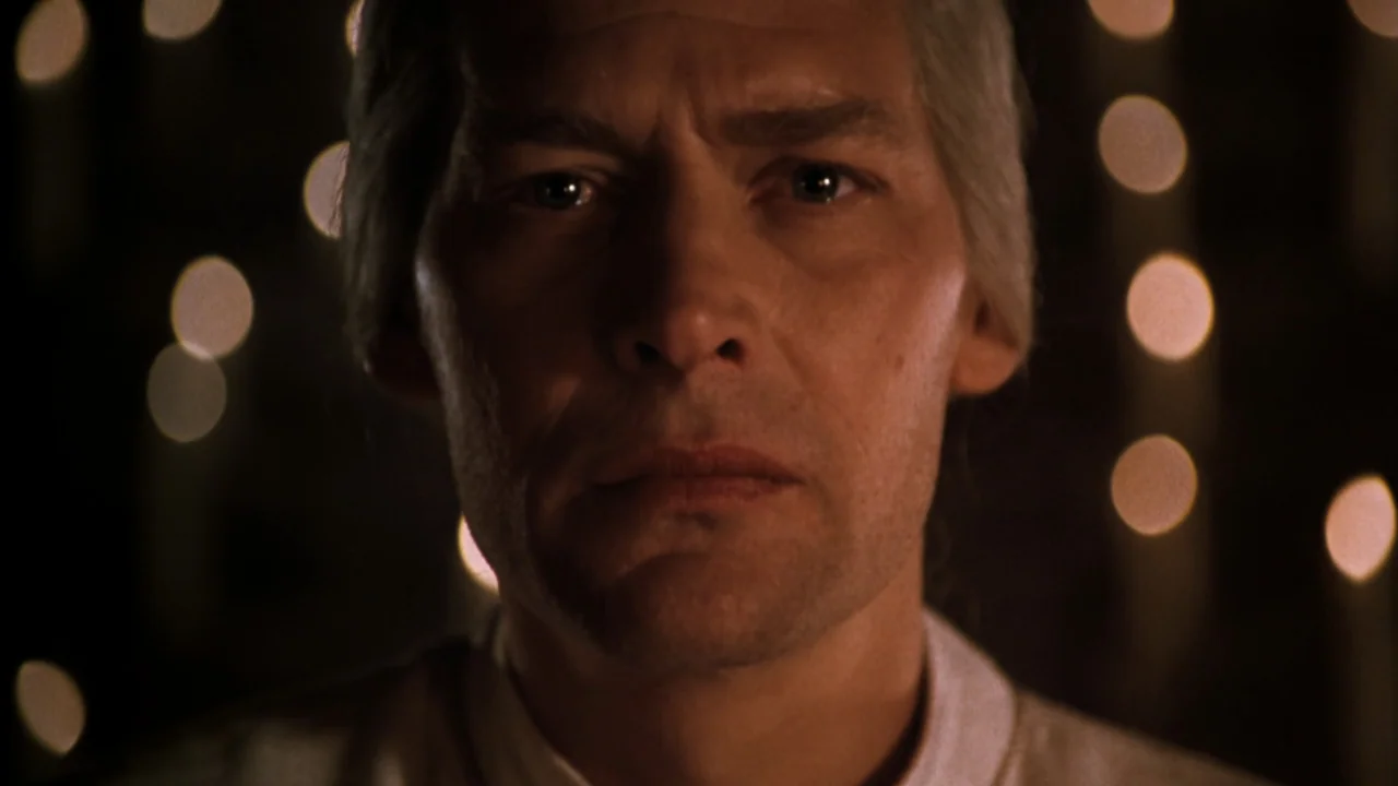 Mortal Kombat: Annihilation (1997) movie still: closeup — A man stands in a dark interior space with numerous small out-of-focus lights behind him.…