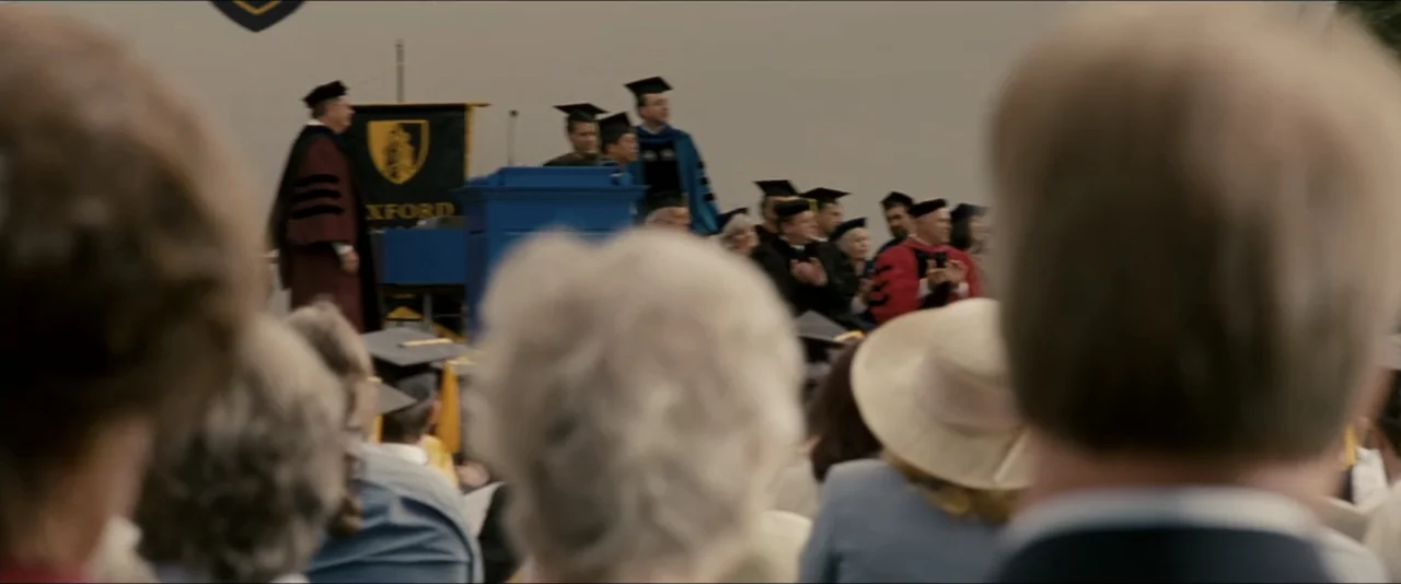 Into the Wild (2007) movie still: wide — An outdoor graduation ceremony features a stage with people in academic regalia. An audience sits in rows…