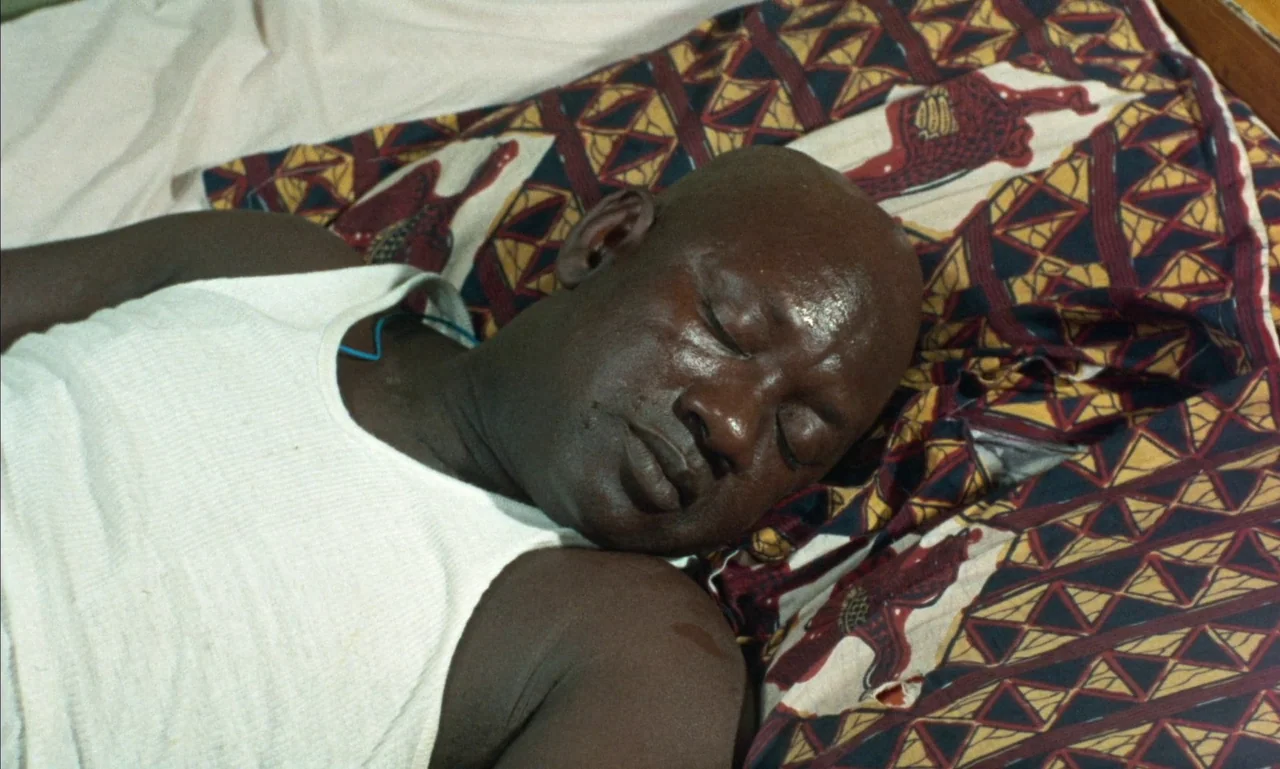 Mandabi (1968) movie still: closeup — A man sleeps on a bed with a patterned geometric fabric covering. The close shot captures the upper body of…
