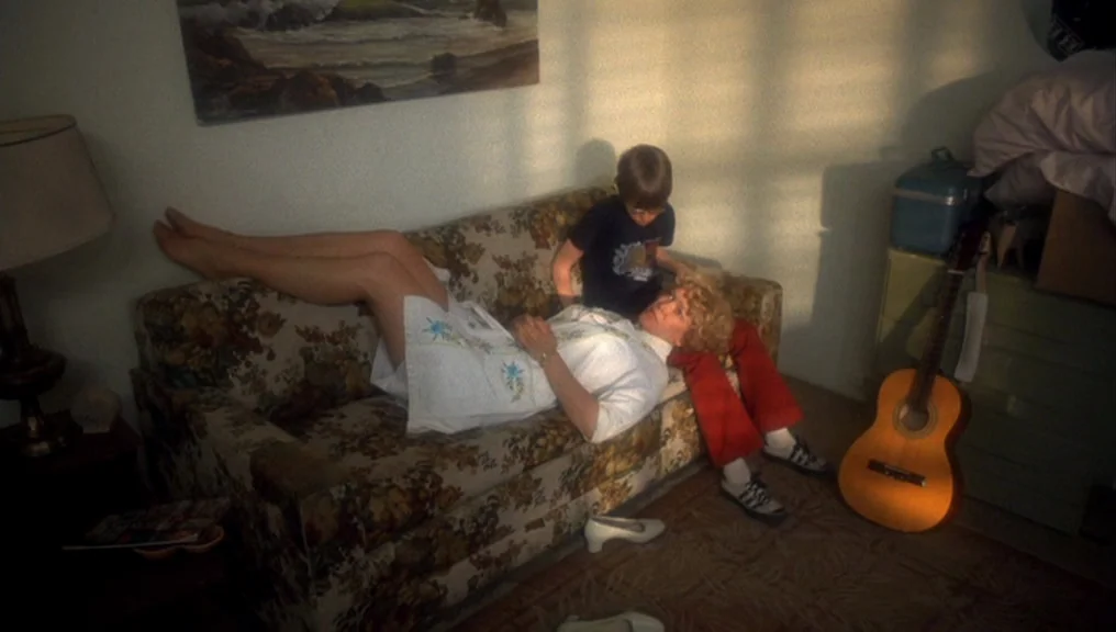 Alice Doesn’t Live Here Anymore (1974) movie still: wide — A living room interior features a floral patterned sofa and a classic acoustic guitar. A…