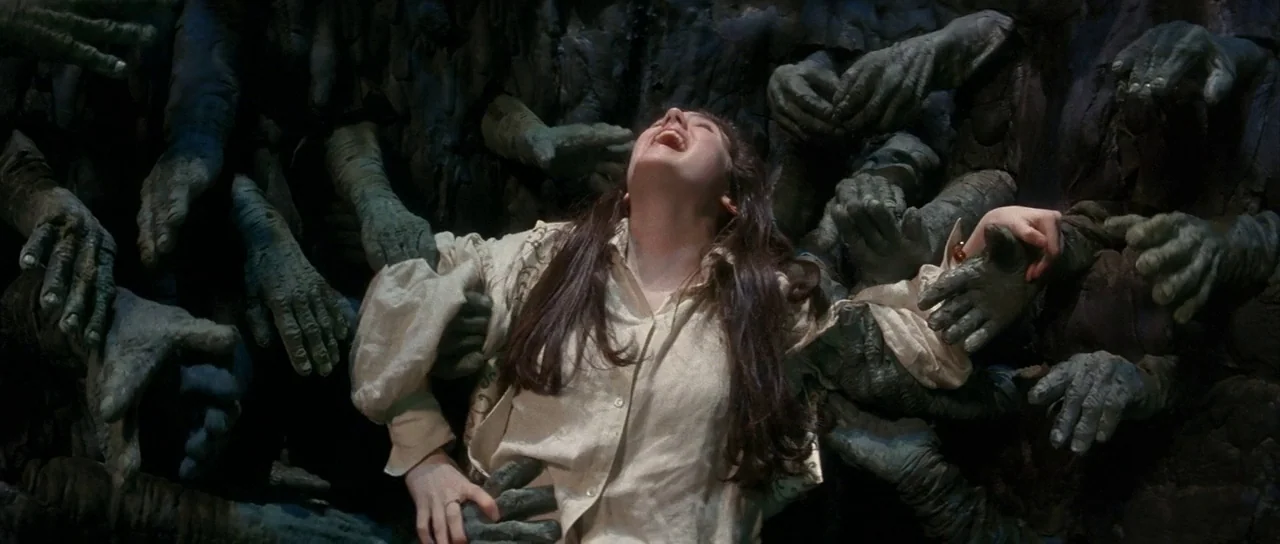 Labyrinth (1986) movie still: medium — A woman is surrounded by numerous dark green, textured hands emerging from a wall. She leans back with her…