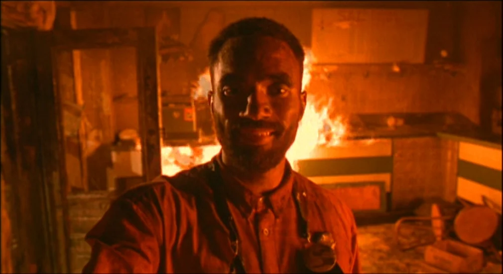 Do The Right Thing (1989) movie still: medium — A pizzeria interior is filled with thick smoke and engulfed in bright flames. A man stands in the…