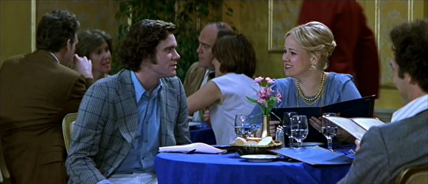 Man On The Moon (1999) movie still: medium — A restaurant interior features a blue-clothed table set for dining with flowers. A man and woman sit…