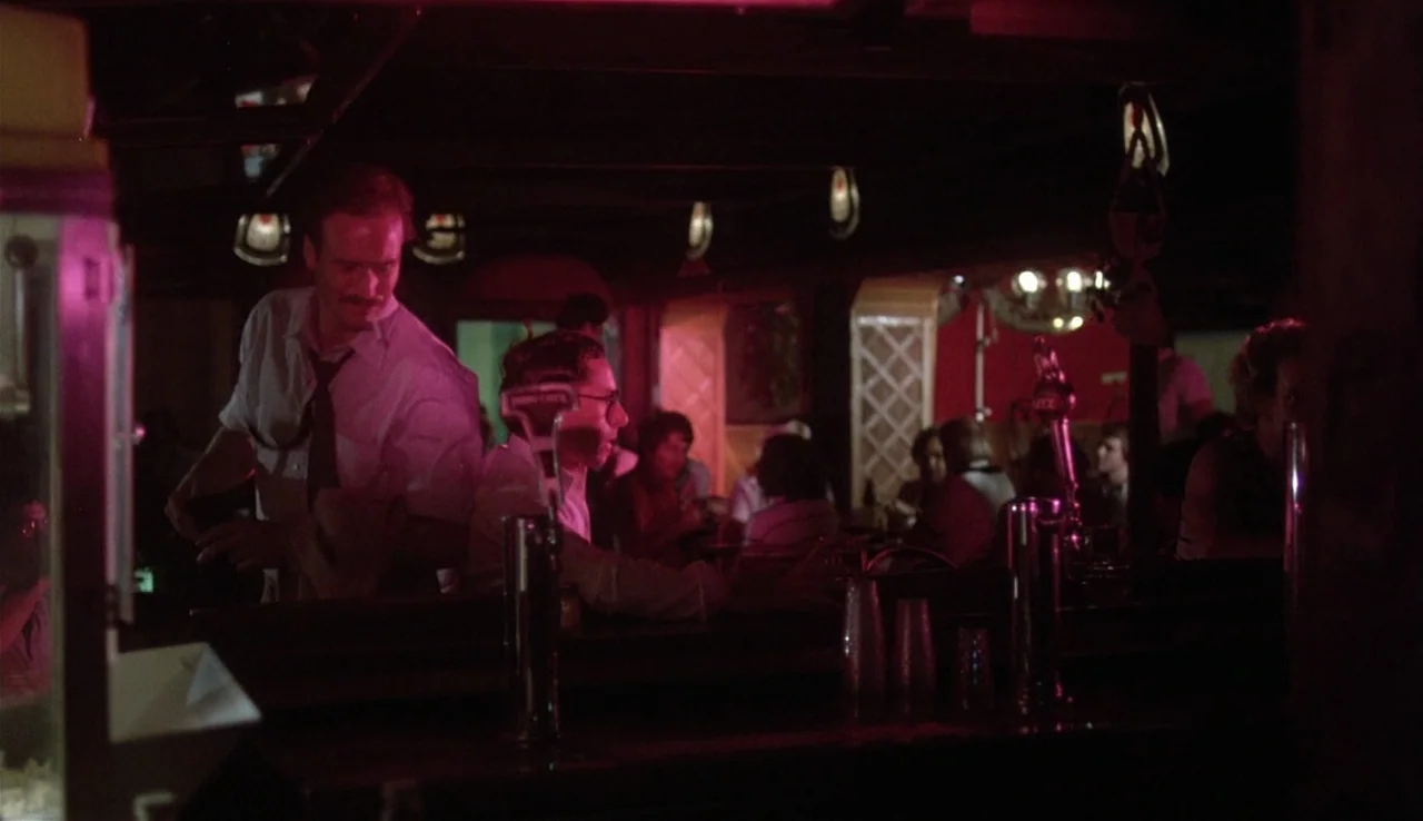 Body Heat (1981) movie still: medium — A dimly lit bar interior features red neon accents and wooden architectural details. A man in a dress shirt…