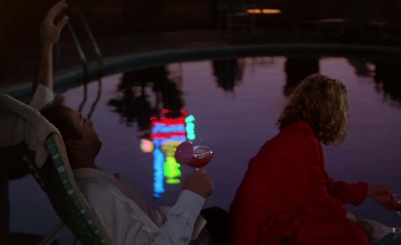 Leaving Las Vegas (1995) movie still: medium — A dark night pool deck reflects colorful neon lights from an off-screen source. A man reclines in a…