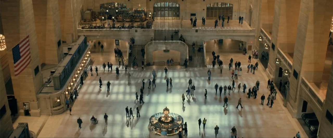Madame Web (2024) movie still: establishing — A high-angle view of a vast, iconic marble train station terminal interior. Numerous people move…