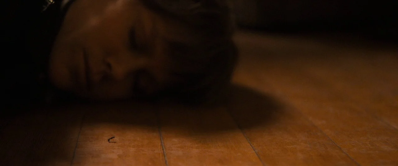 Destroyer (2018) movie still: closeup — A person lies with their cheek against the planks of a dark wooden floor. The individual has their eyes…
