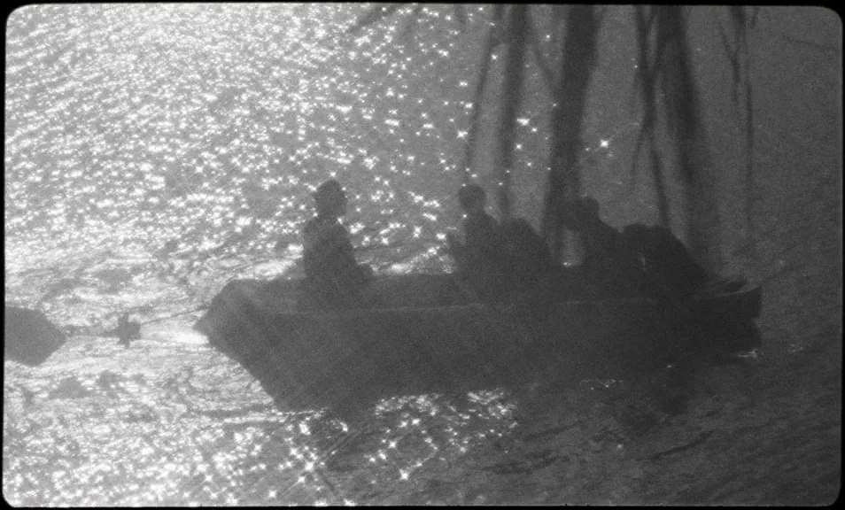 The Wild Boys (2017) movie still: wide — A small rowboat carrying several figures floats across a bright, shimmering expanse of water. The figures…