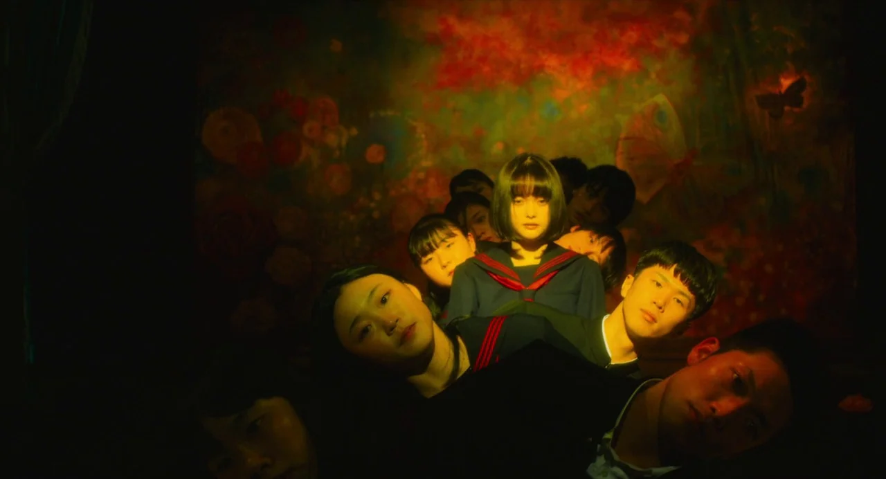 Diner (2019) movie still: medium — A dark, dimly lit room contains a large abstract floral wall mural behind them. A group of teenagers with neutral…
