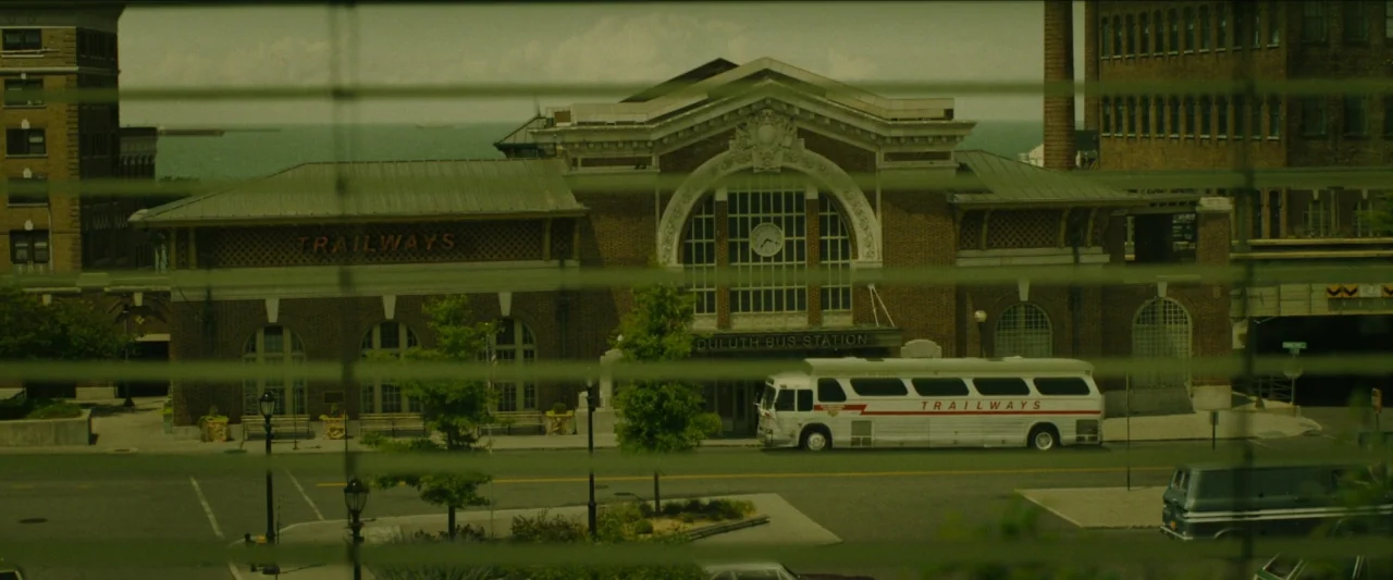 Wonderstruck (2017) movie still: establishing — A brick bus station sits on a quiet street behind Venetian window blinds. A vintage white and red…