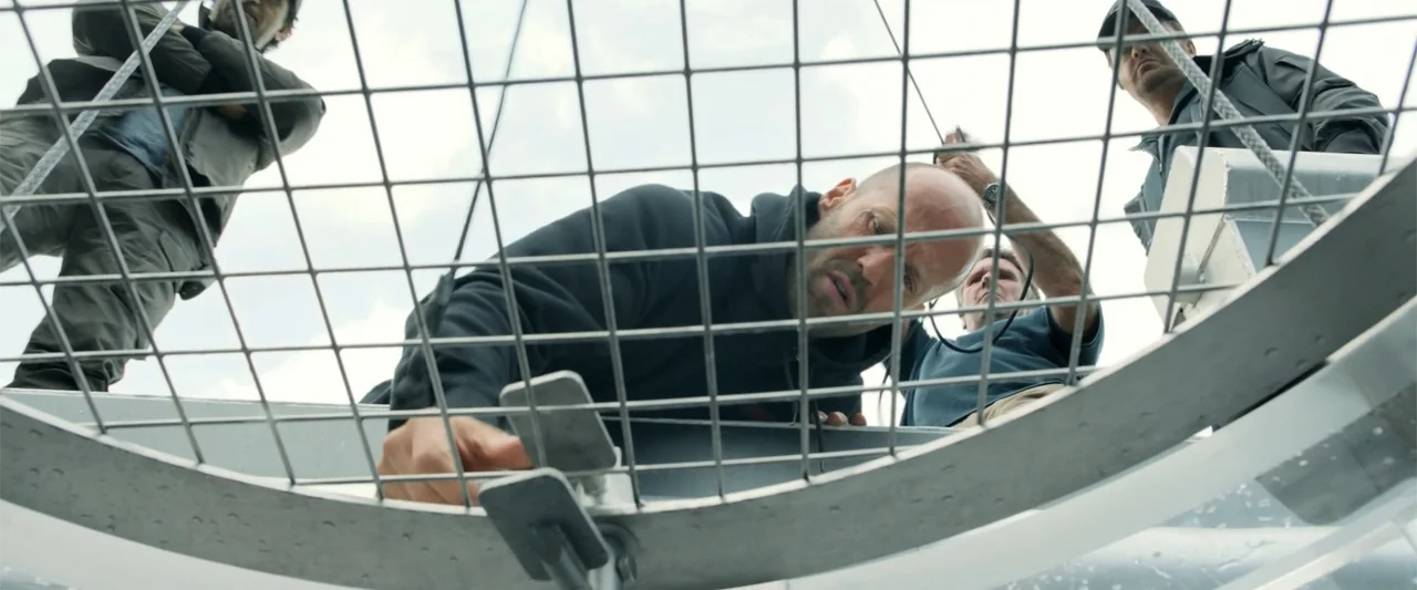 The Meg (2018) movie still: medium — A group of men stand around a circular opening covered by a metal grate. They look down into the gap while…