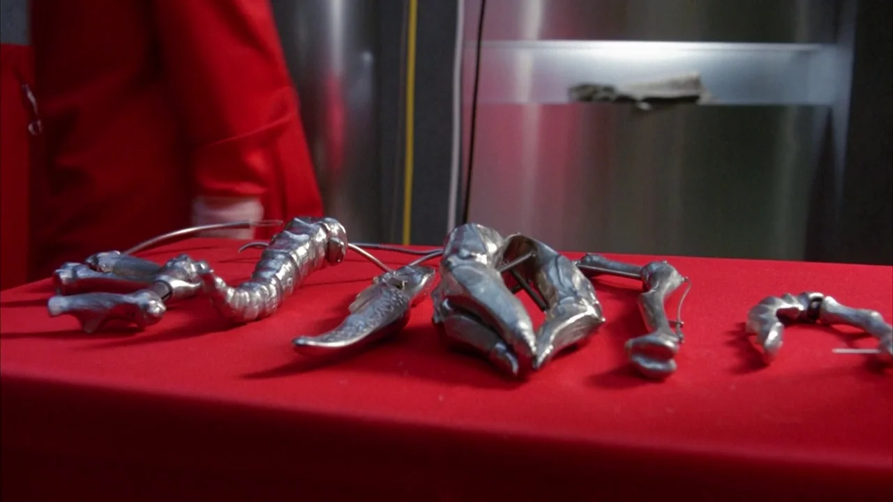 Dead Ringers (1988) movie still: closeup — A collection of silver metallic surgical tools sits arranged on a bright red tablecloth. A stainless…