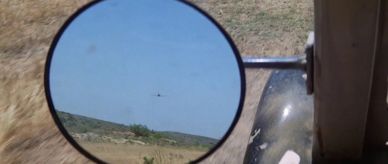 Indiana Jones and the Last Crusade (1989) movie still: closeup — A circular side mirror of a vehicle reflects a vast blue sky and dry terrain. A…