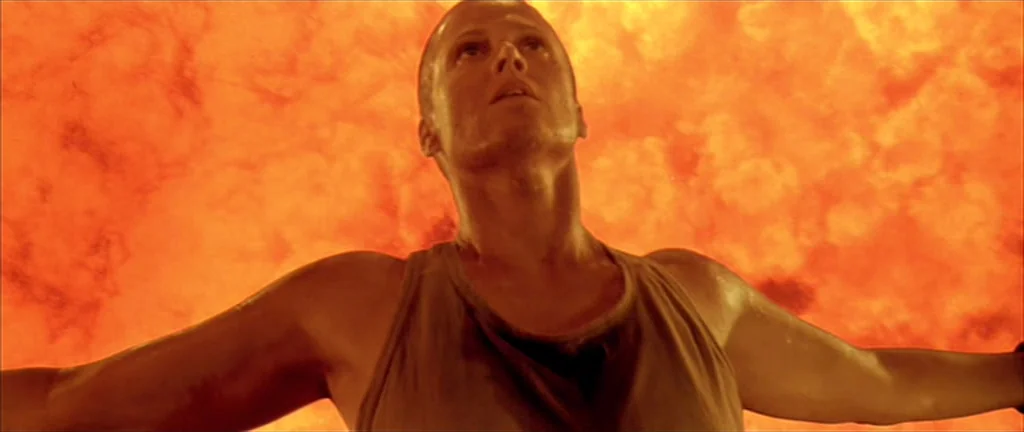 Alien 3 (1992) movie still: medium — A woman stands before a wall of intense fire within a dark environment. She falls backward with her arms…