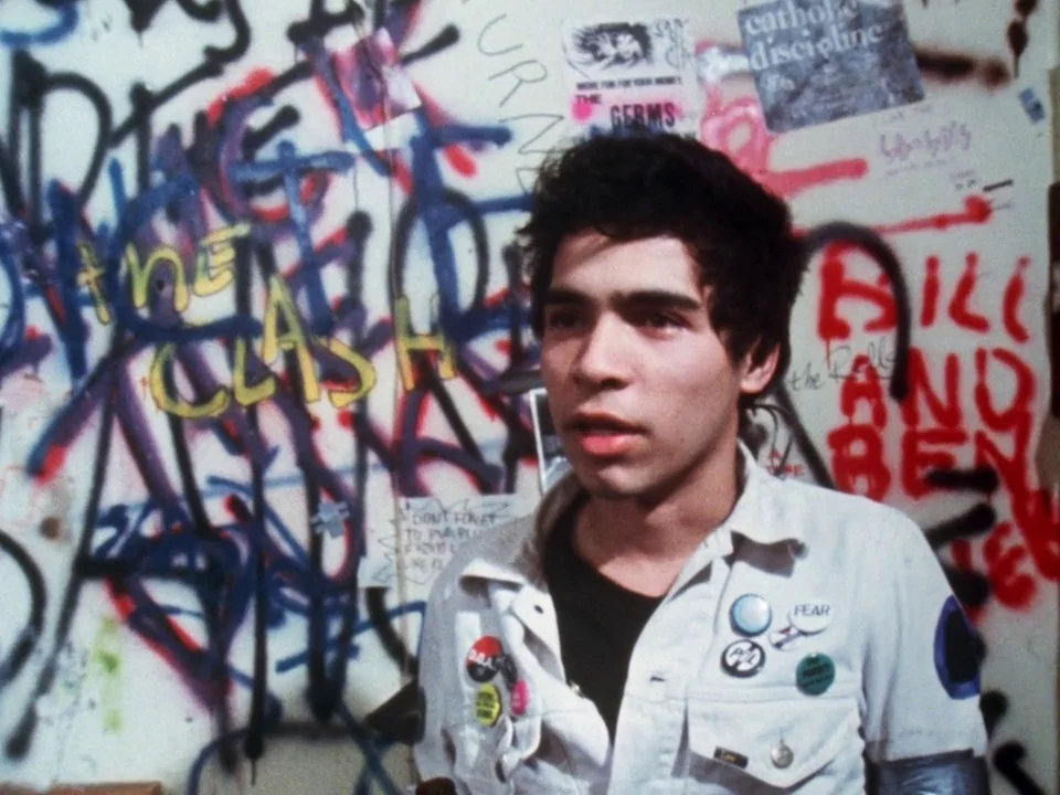 Decline of Western Civilization (1981) movie still: medium — A wall covered in layers of colorful spray-painted graffiti and various music posters.…