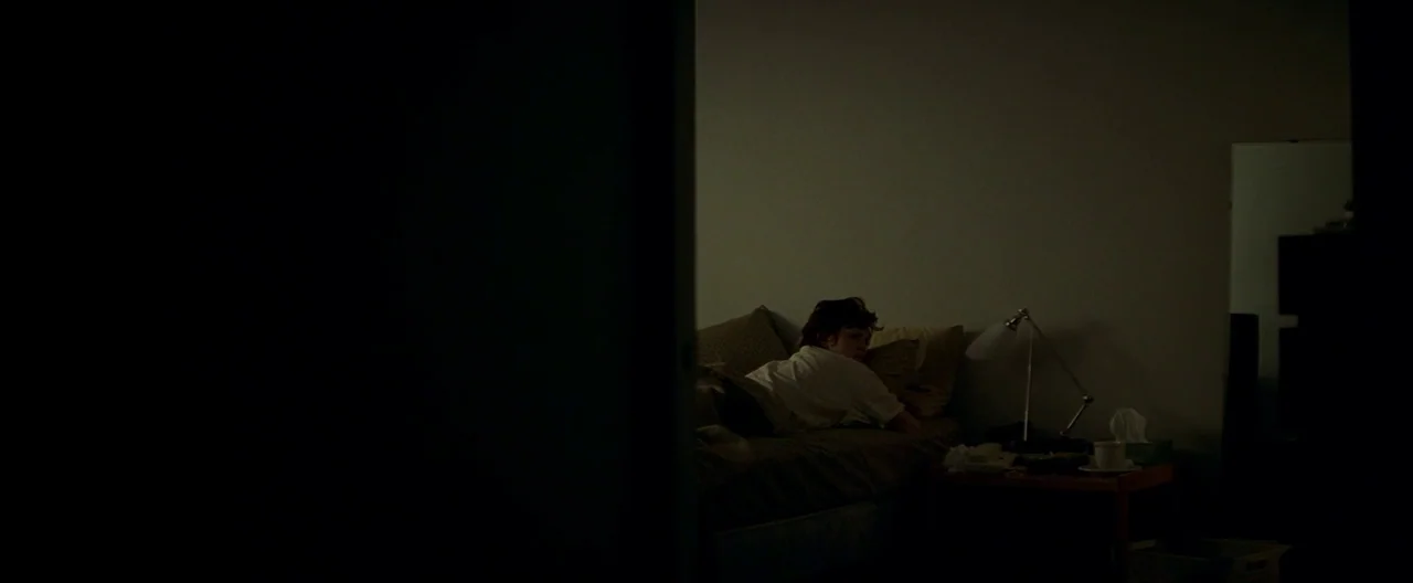 The Yards (2000) movie still: wide — A dimly lit room at night seen from a doorway. A person lies in bed next to a lit desk lamp.