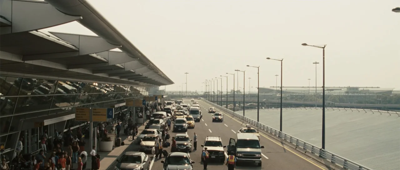 Going the Distance (2010) movie still: establishing — An elevated road runs alongside a modern glass and steel airport terminal building. Numerous…