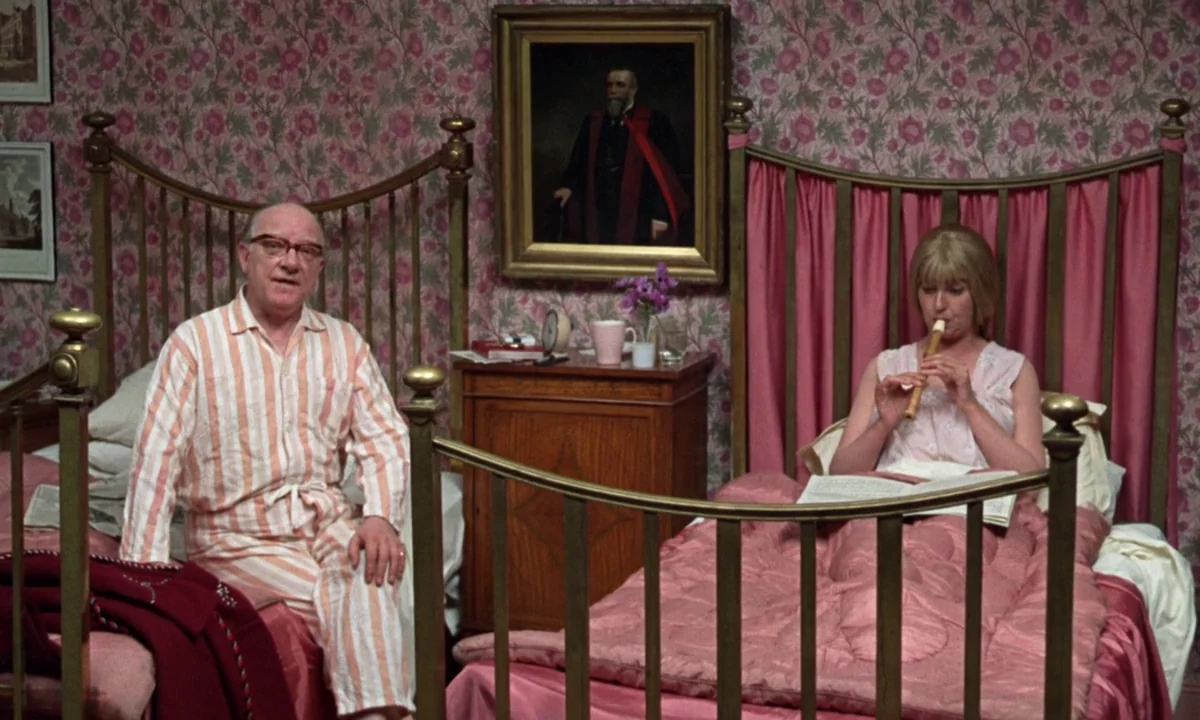 If…. (1968) movie still: wide — A bedroom features floral pink wallpaper, two matching twin beds, and a framed oil portrait. A man in pajamas sits…