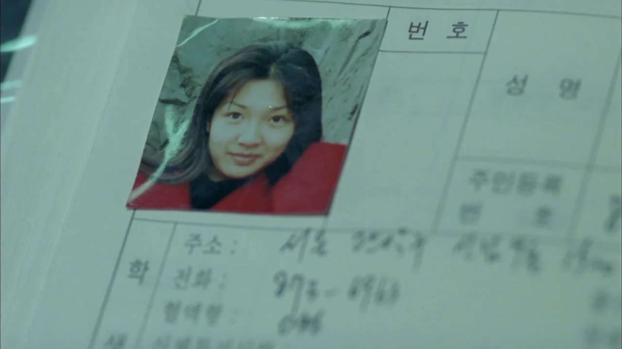 Whispering Corridors (1998) movie still: closeup — A close-up view shows a woman's photograph attached to a paper form. The document has handwritten…