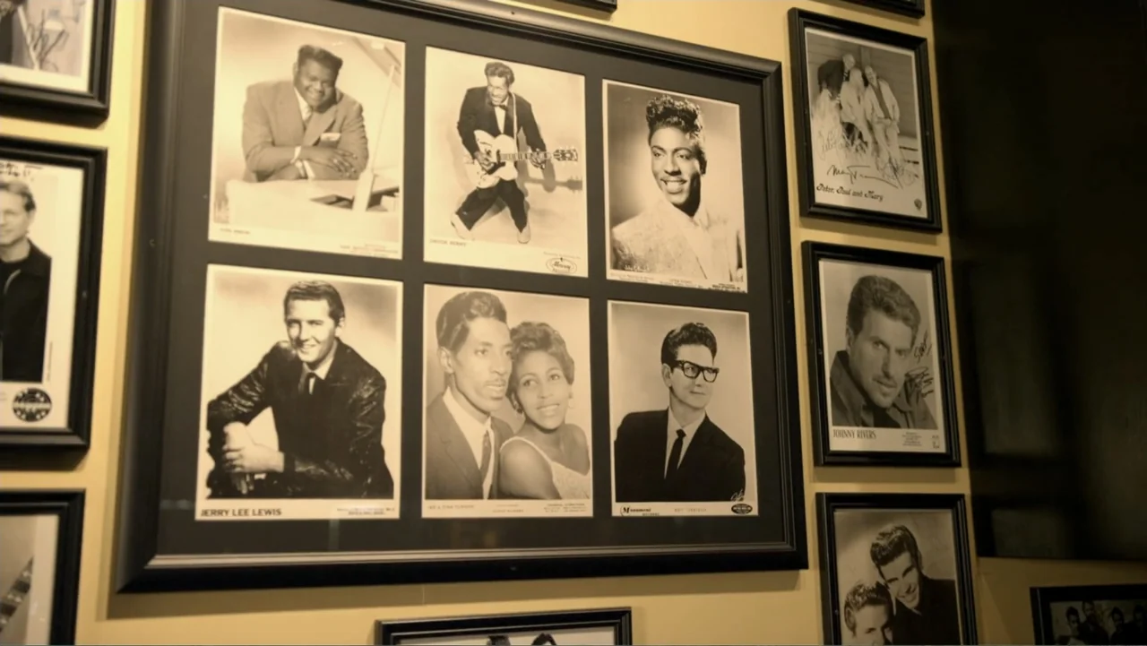 The Day the Music Died: The Story of Don McLean's "American Pie" (2022) movie still: medium — A cream-colored wall displays several black-and-white…