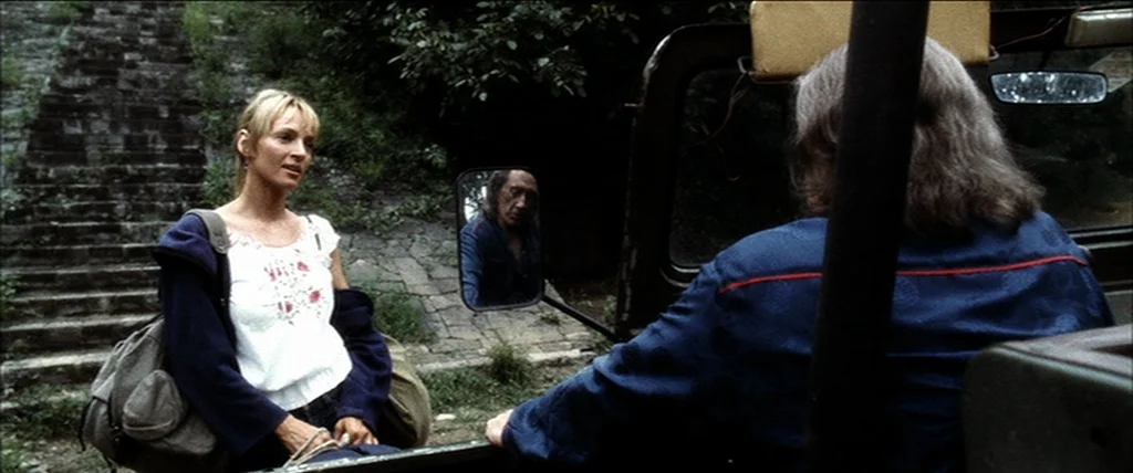 Kill Bill Vol. 2 (2004) movie still: medium — A woman stands on a stone pathway next to a vintage off-road vehicle. She speaks to the driver who is…